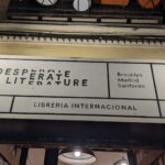 Rótulo de la librería Desperate Literature rodeado de dos faroles cuadrados encendidos. El texto dice "Desperate Literature / Brooklyn, Madrid, Santorini / Librería internacional".
