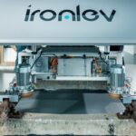 Dos ingenieros de IronLev preparan su vehículo autónomo de pseudolevitación magnética sobre un trozo de vía ferroviaria en un laboratorio.