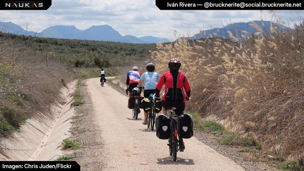 Charla "La maldición de la pata de mono", Naukas Guardo 2024, diapositiva 32. Vía verde (antigua vía férrea acondicionada como camino) con ciclistas alejándose de la cámara.