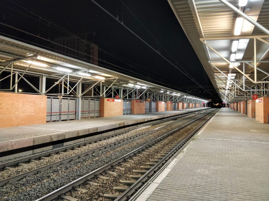 Vista nocturna en perspectiva de la estación de Las Retamas en la línea C-5 de Cercanías Madrid. Los andenes están vacíos. Se aprecia tanto la vía con su cable radiante de LZB entre los raíles como la catenaria. También se ve que no hay señales verticales a la salida de la estación, como debería ser el caso si se tratara de un límite de cantón ASFA.