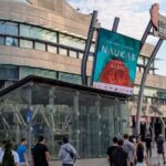 Público aproximándose al palacio Euskalduna para asistir a una sesión del evento Naukas Bilbao. Se ve parte del edificio y su pantalla anunciadora con el cartel del evento.