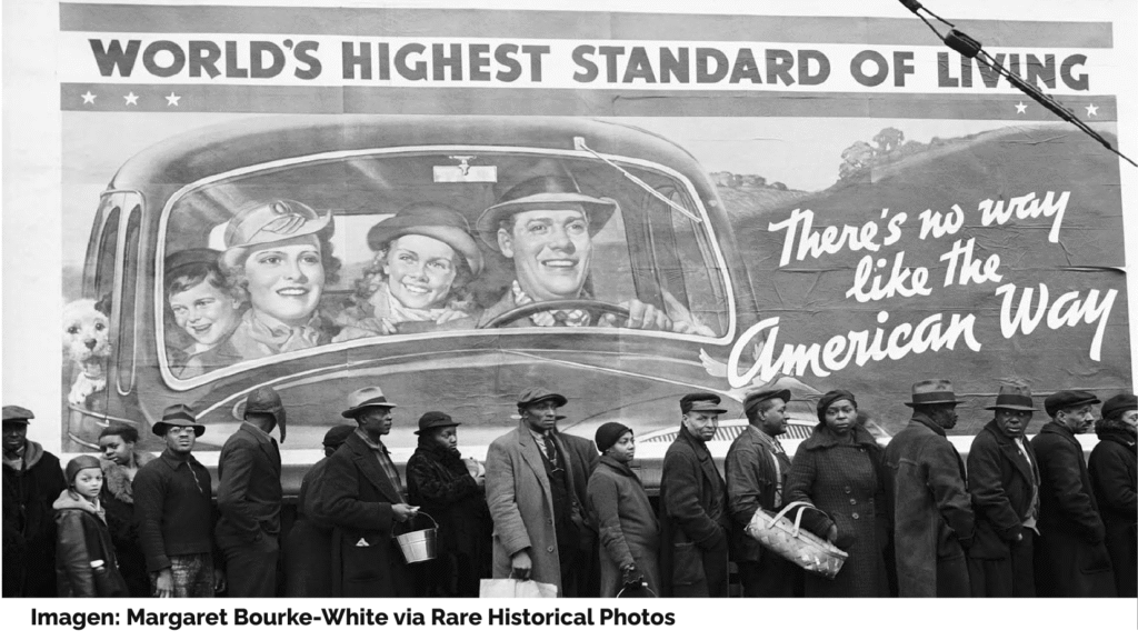 Una cola de personas negras (hombres, mujeres, niños) esperan frente a una gran valla publicitaria en la que, bajo el mensaje "World's highest standard of living" y "There's no way like the American Way" una familia acomodada de personas blancas (marido, esposa, niña, niño, perro) circula en un coche. Imagen: Margaret Bourke-White, Rare Historical Photos.