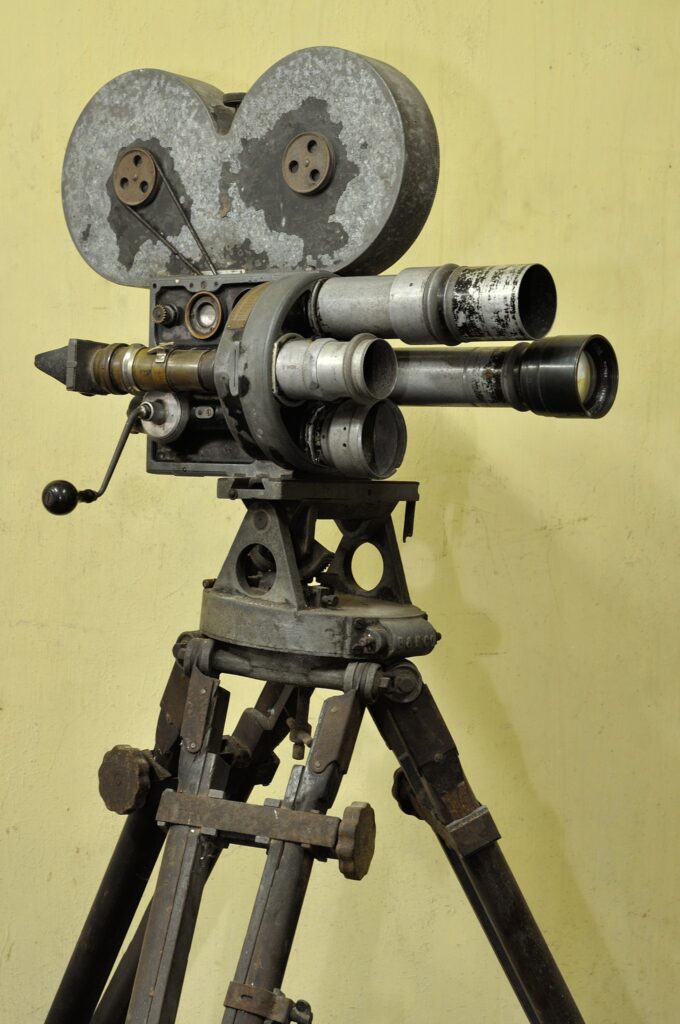 Una cámara cinematográfica con trípode, de la década de 1920, que ha visto mejores tiempos. Está muy usada.