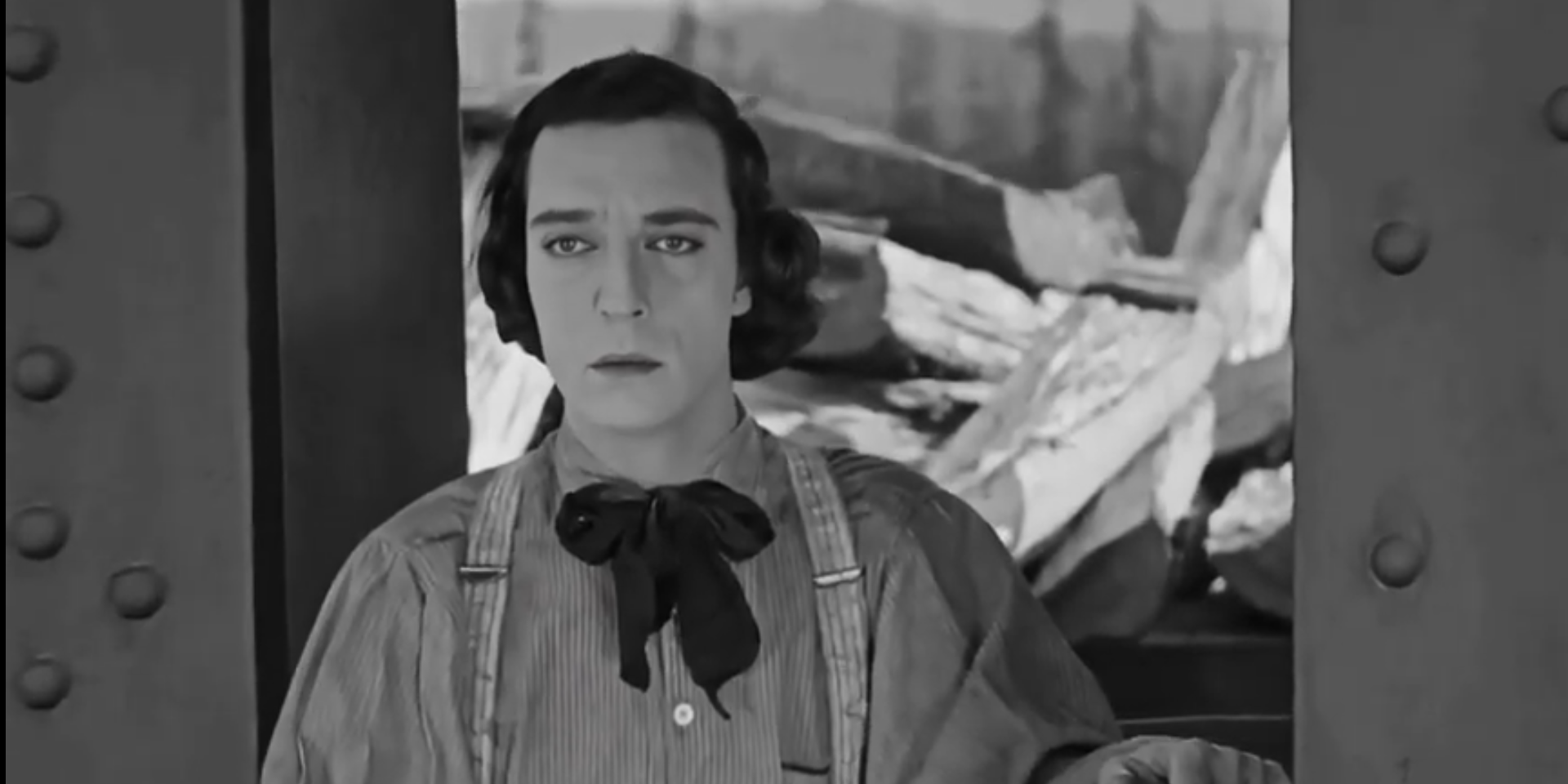 Buster Keaton, caracterizado como Johnnie Gray en El maquinista de La General, mira hacia delante con cara de ligero fastidio. Lleva un atuendo típico de mediados del siglo XIX para un maquinista: camisa, tirantes y un lazo negro en el cuello.
