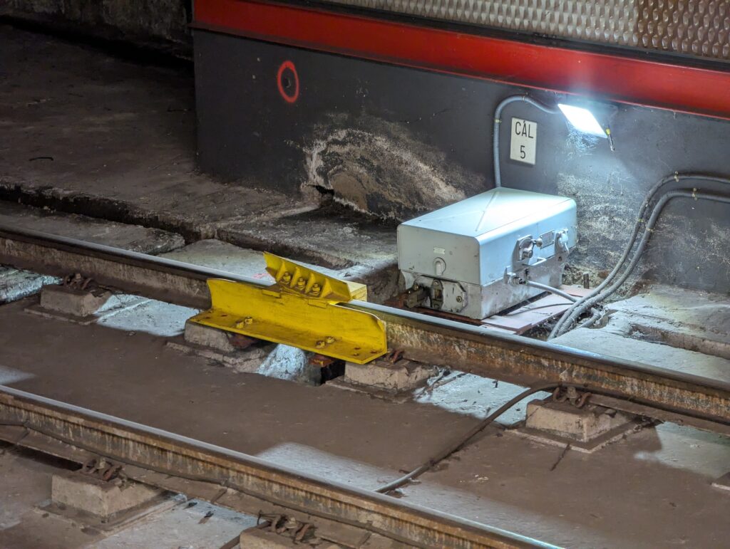 En un raíl se observa un dispositivo de color amarillo que levanta la rueda de cualquier tren que pase sobre él (de derecha a izquierda) y dirige su pestaña hacia el exterior de la vía. Esto provocaría un descarrilamiento inmediato que, si ocurre a baja velocidad (en una vía secundaria no suele ser posible alcanzar velocidades altas), estará controlado, quedando el tren parado y de pie.