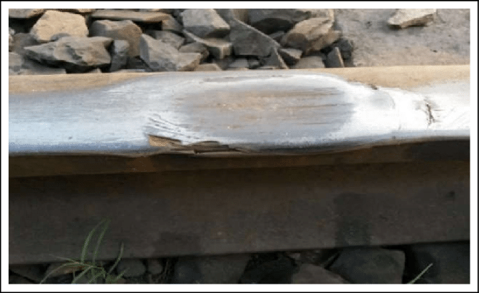 Un primer plano de un raíl ferroviario. En su cabeza (la parte superior) se ve una abolladura provocada por una rueda que ha girado sin avanzar en ese punto, calentando el metal y deformándolo.