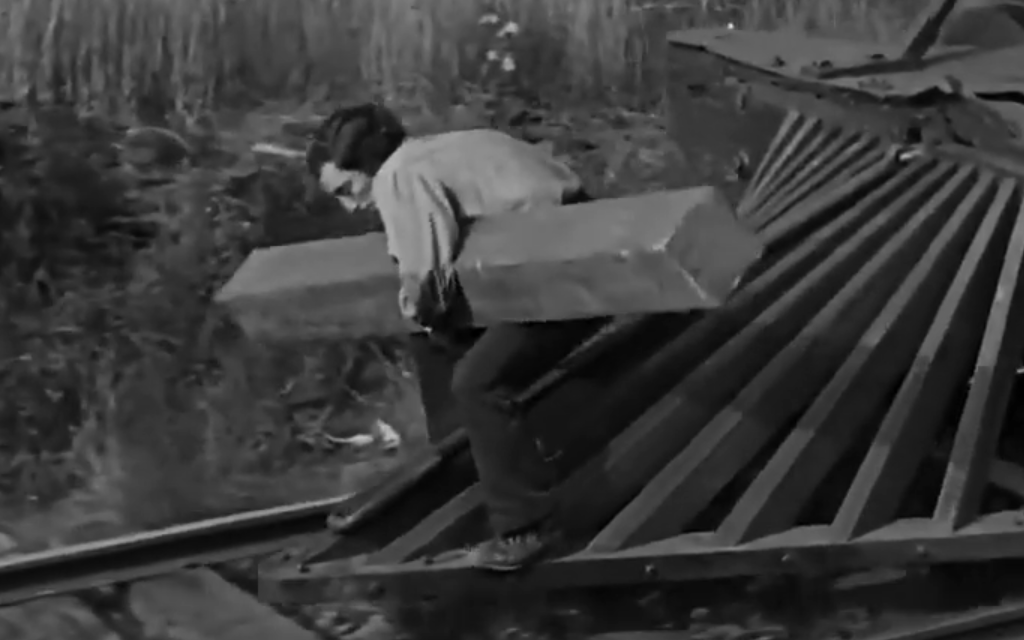 Keaton sostiene una traviesa con un brazo mientras hace equilibrios sobre el apartavacas de su locomotora en El maquinista de La General.