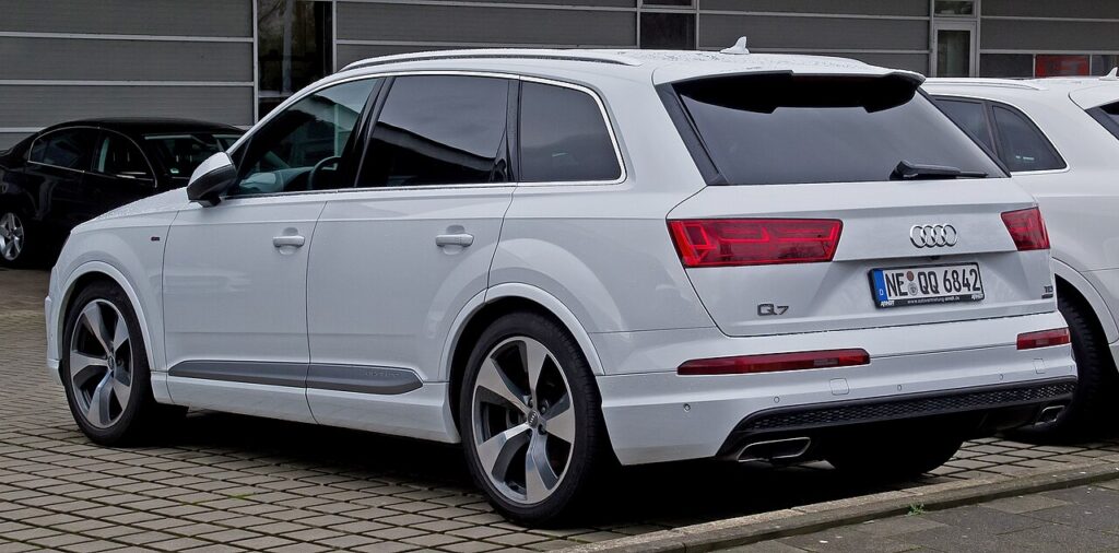 Audi Q7 en vista de tres cuartos desde atrás y la izquierda. Es un cocharráncano de más de cinco metros de longitud, innecesariamente grande y ostentoso. Este ejemplar concreto es de color blanco.
