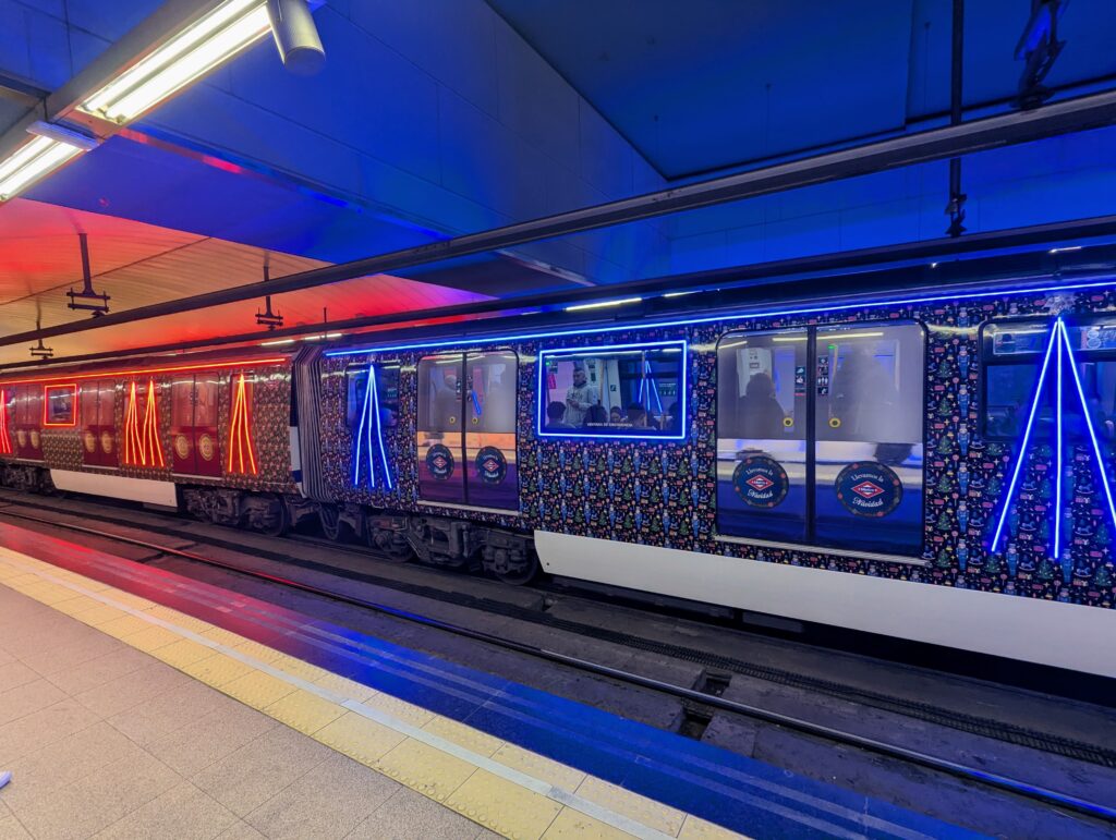 Un tren de la serie 3000 en la línea 3 de Metro de Madrid, vinilado con un patrón de motivos navideños y con cintas led de colores azul y rojo formando vértices sobre algunas ventanas y enmarcando otras.