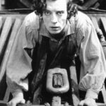 Buster Keaton mira al frente encaramado a cuatro patas en el apartavacas de una locomotora de vapor, en una imagen promocional para El maquinista de La General.