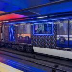 Un tren de la serie 3000 en la línea 3 de Metro de Madrid, vinilado con un patrón de motivos navideños y con cintas led de colores azul y rojo formando vértices sobre algunas ventanas y enmarcando otras.